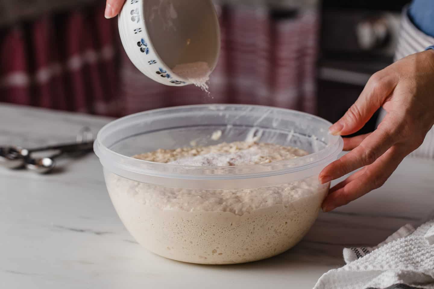 A woman adding salt, baking powder and baking soda to a bowl of dough.
