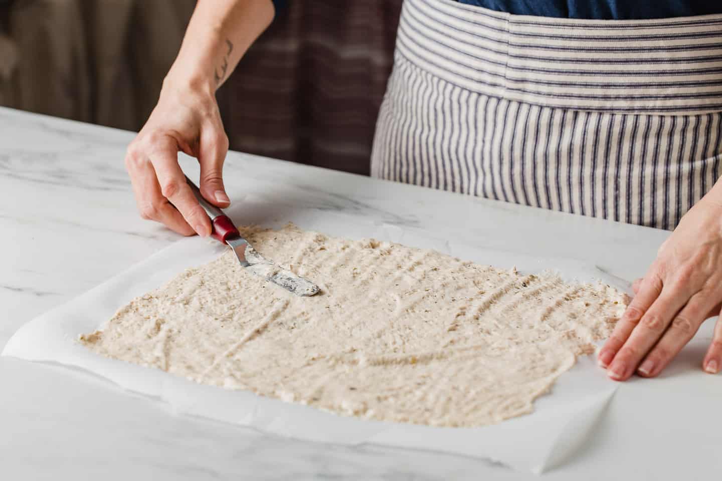 A woman spreading the batter onto a piece of parchment paper.
