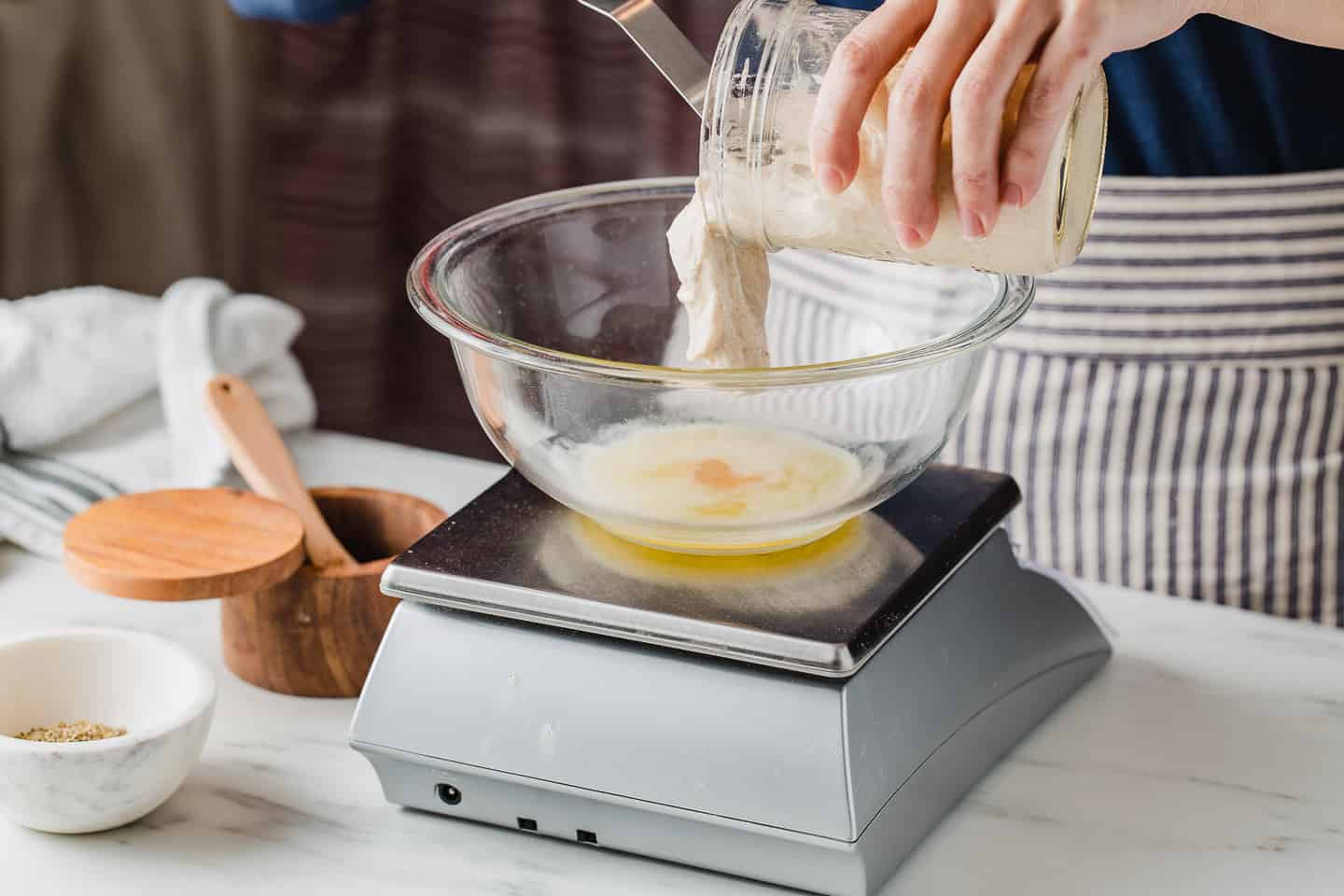 A woman weighing sourdough discard ingredients with a kitchen scale.