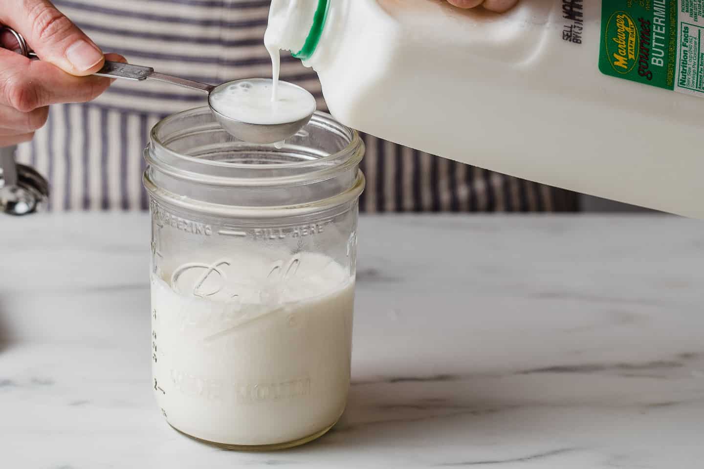 A woman adding cultured buttermilk to heavy cream in a jar.
