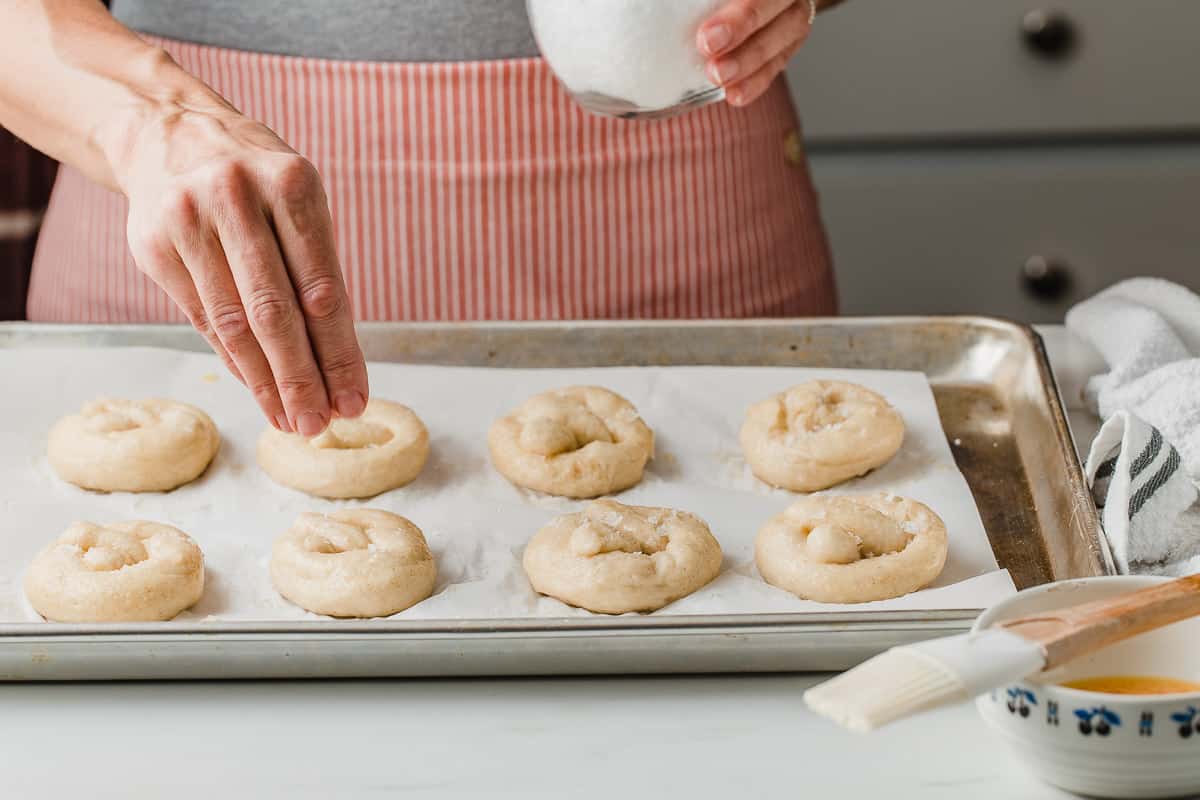 A woman sprinkling salt on pretzel dough.
