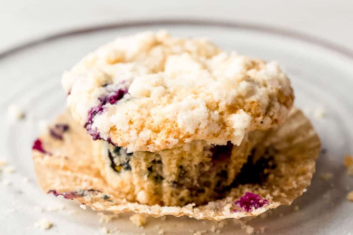 A blueberry muffin in it's wrapper on a plate.