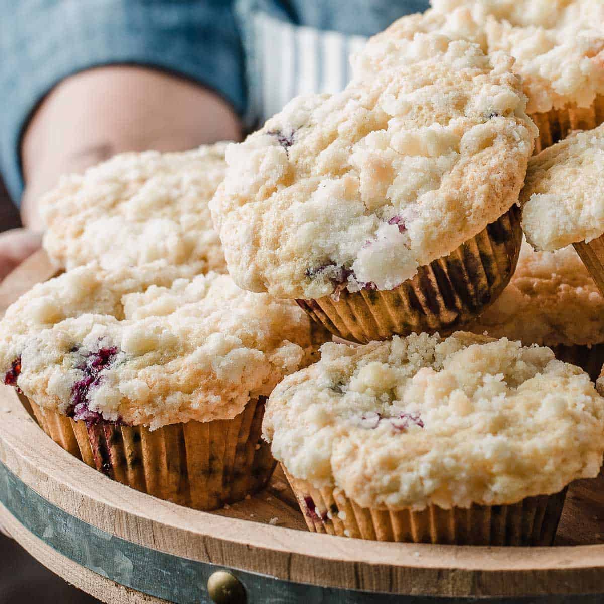 A woman holding a tray of sourdough blueberry muffins.