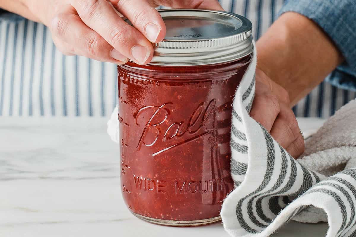 A woman placing the lid on a jar of strawberry jam.
