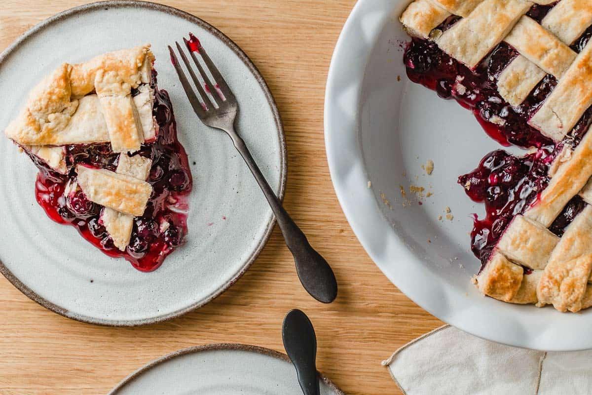 An over head picture of a blueberry pie with two slices on plates.
