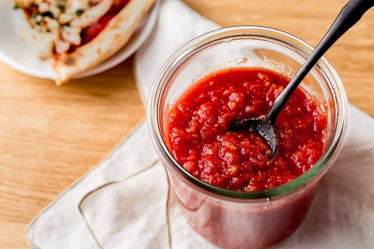 Neapolitan style pizza sauce in a jar with a spoon.