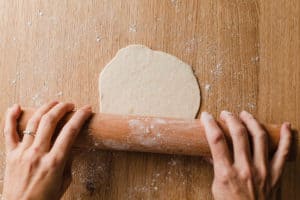 A woman rolling out sourdough tortilla dough with a rolling pin.