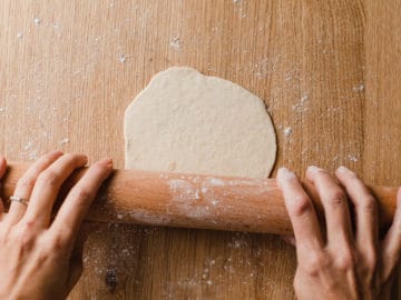 A woman rolling out sourdough tortilla dough with a rolling pin.