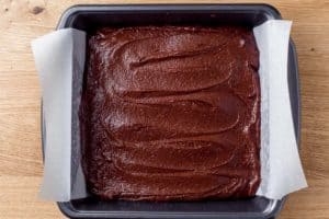 Brownie batter in a baking dish lined with parchment paper.