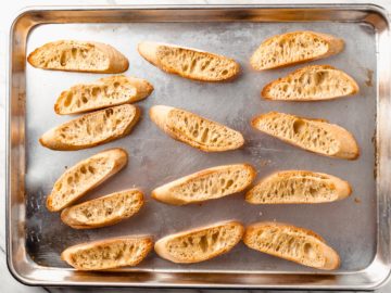 Slices of toasted baguette on a baking sheet.