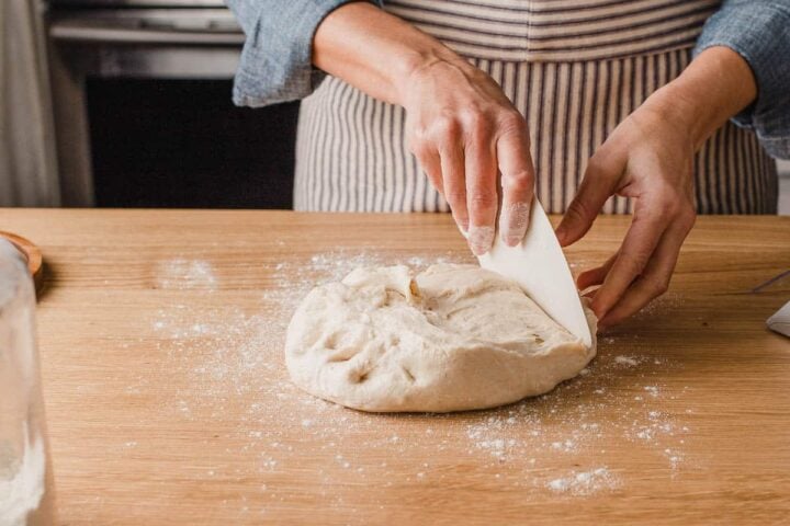 A woman dividing dough with a bench scraper.