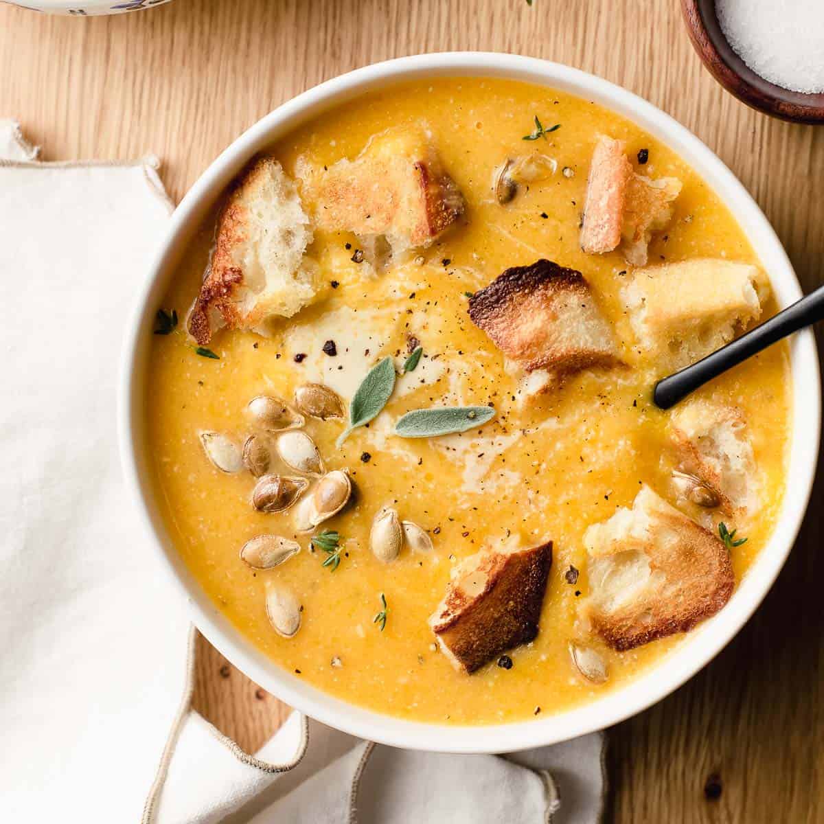 A bowl of roasted butternut squash soup with croutons and roasted seeds in a bowl.
