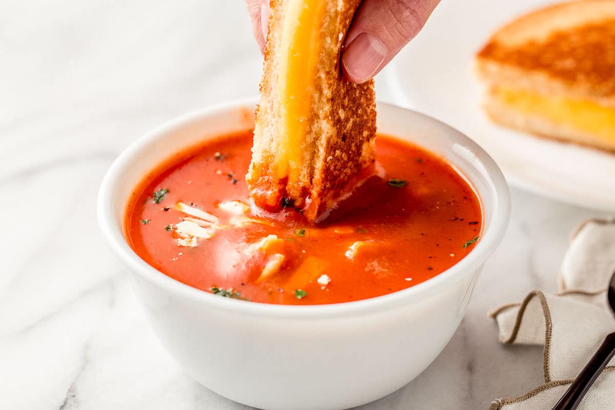 A grilled cheese sandwich dunked into a bowl of tomato soup.