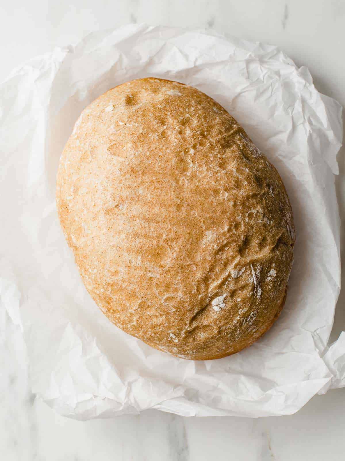 A loaf of slow cooker sourdough bread on a piece of parchment paper.
