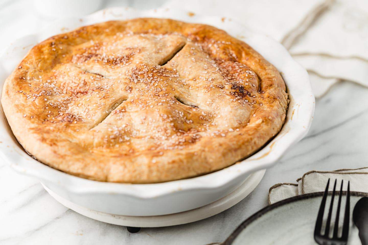 Deep dish apple pie with an all-butter pie crust sitting on a trivet.