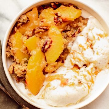 Peach crisp in a bowl with ice cream.