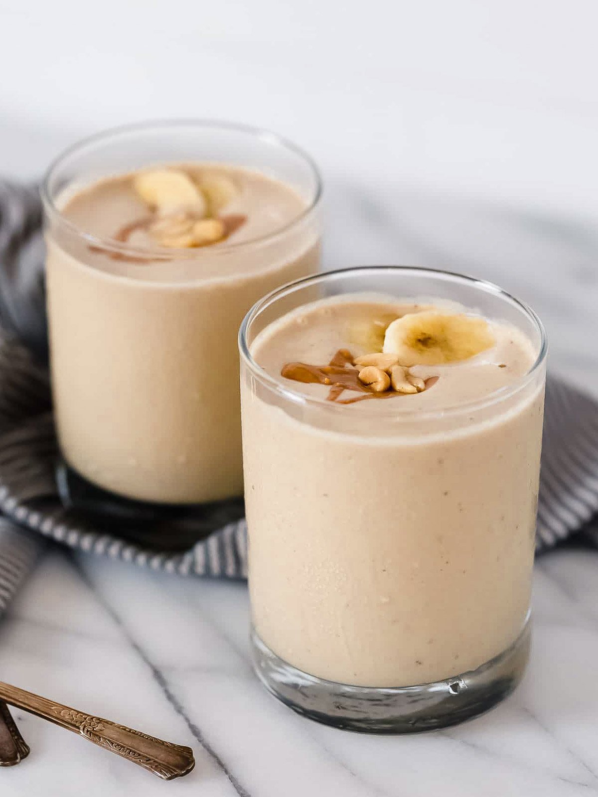 Peanut butter banana smoothies in glasses on a countertop.