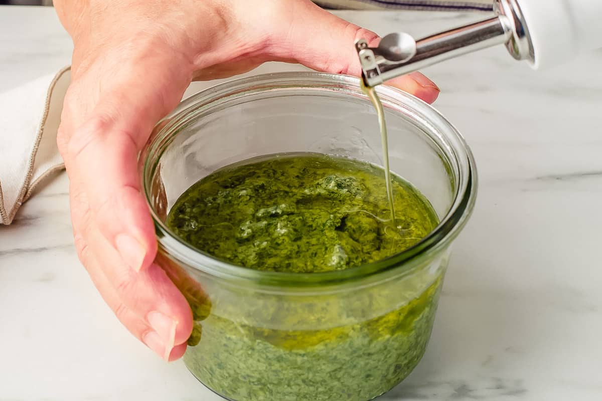 Pouring olive oil on top of Basil pesto.