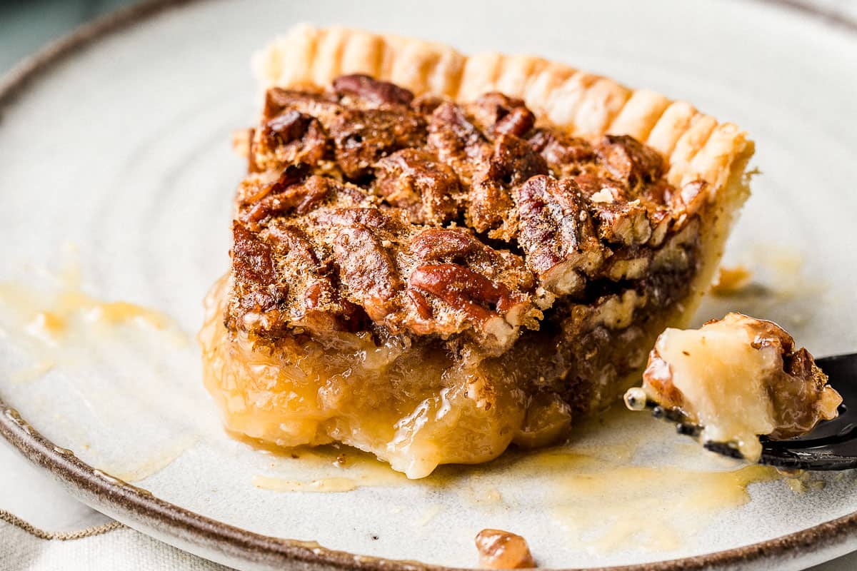 A slice of pecan pie on a plate with a bite taken out.