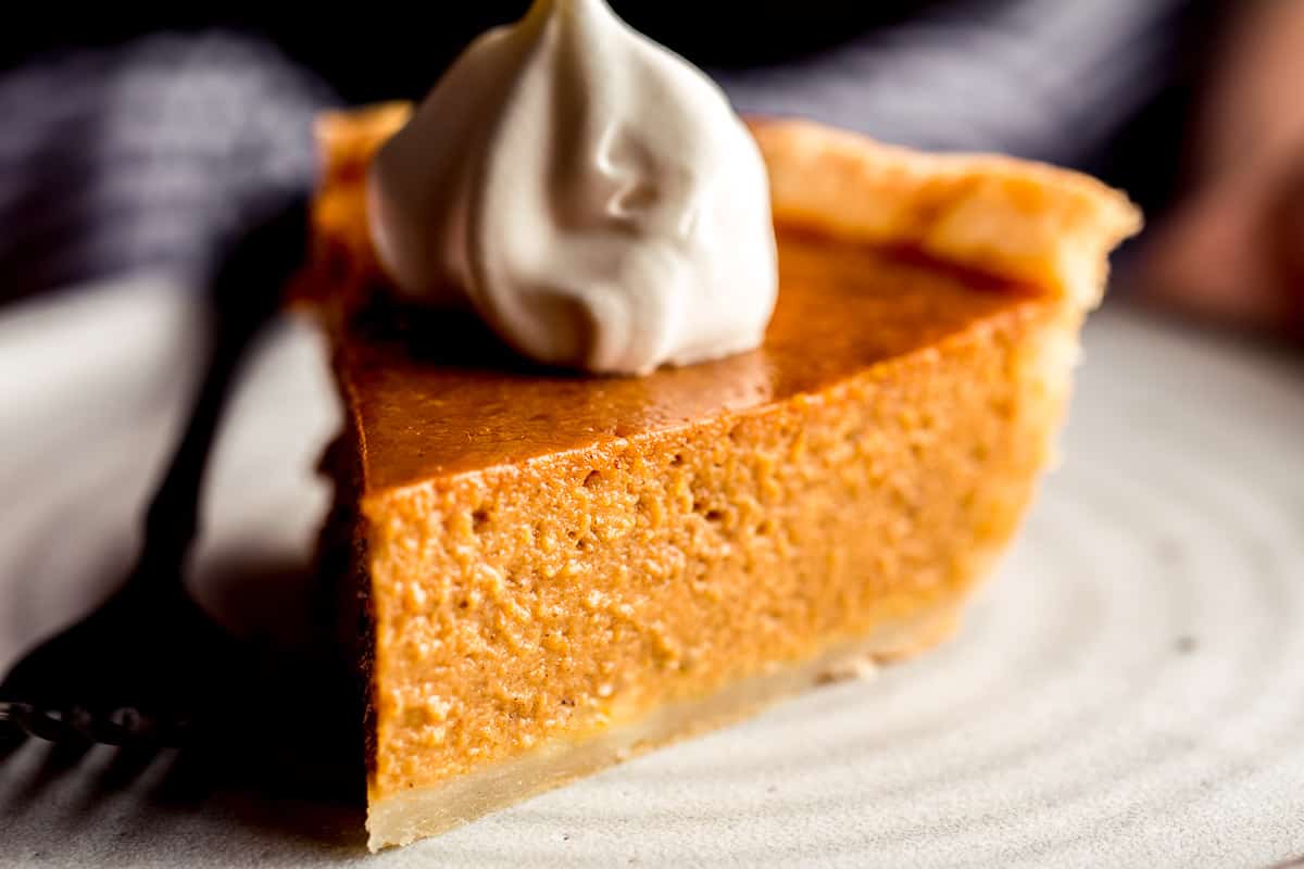 A woman holding a slice of pumpkin pie on a plate.