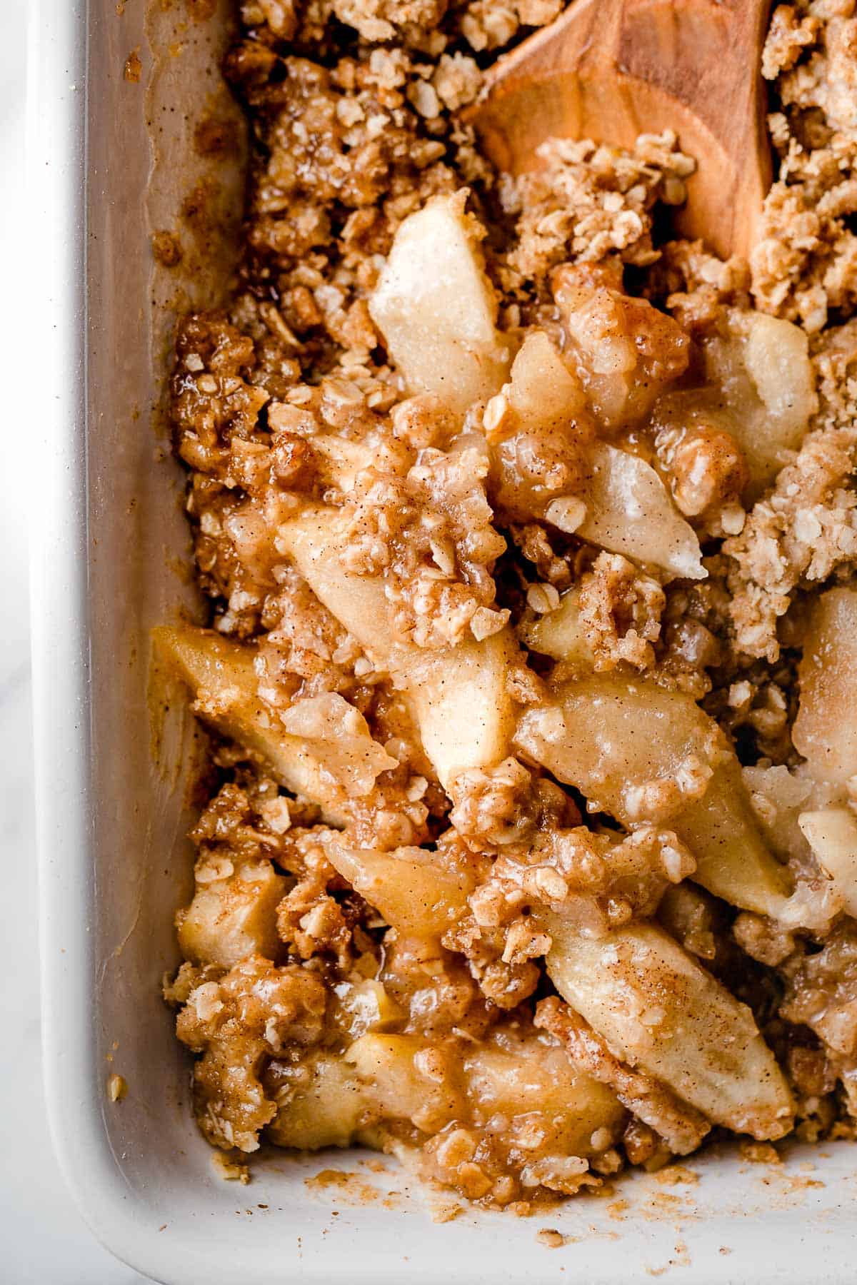 A baking dish with baked apple crisp and a serving spoon.