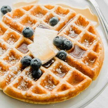 A gluten free waffle on a plate with butter and syrup.