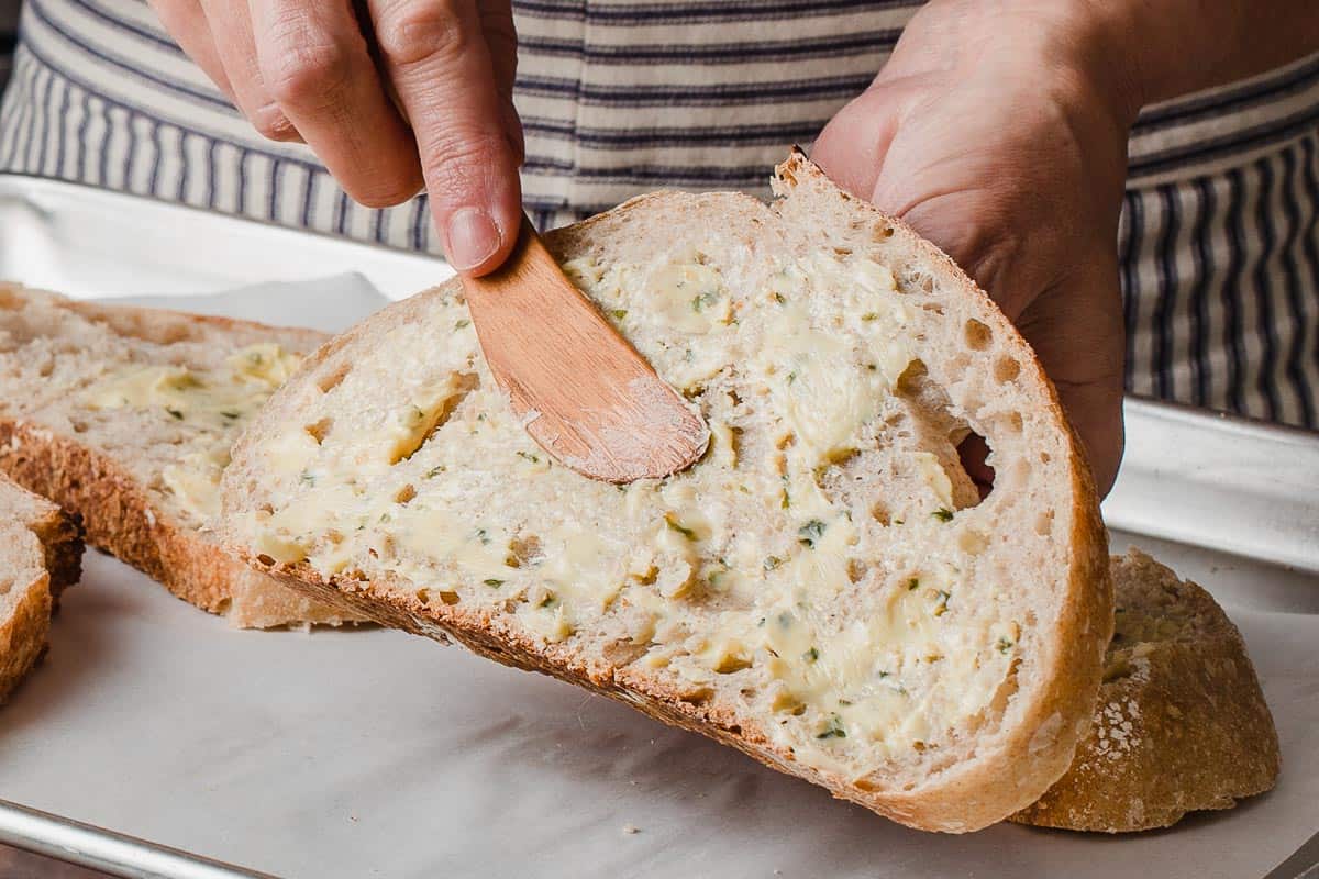 A person spreading herb butter on sourdough bread.