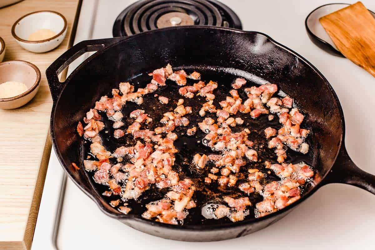 Bacon cooking in a cast iron skillet on the stovetop.
