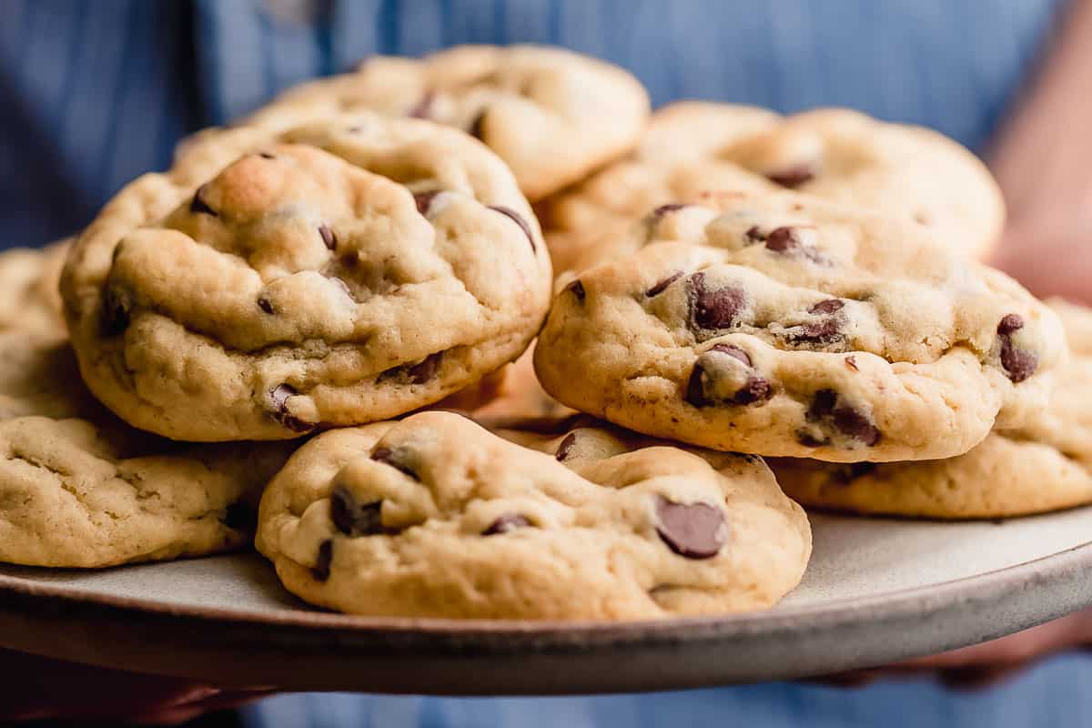 A person holding a plate of chocolate chip cookies.