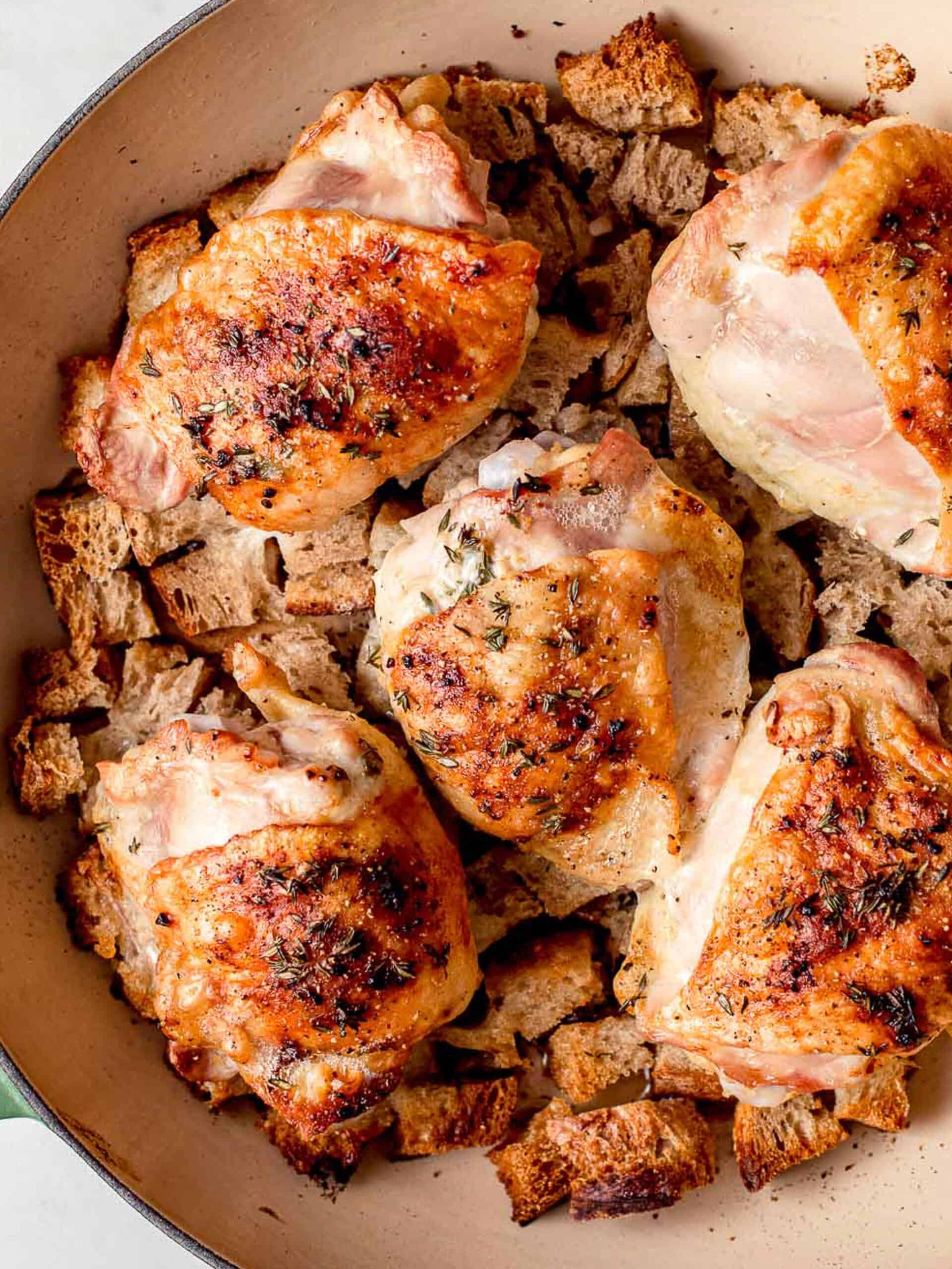 Baked chicken thighs with croutons in a skillet.
