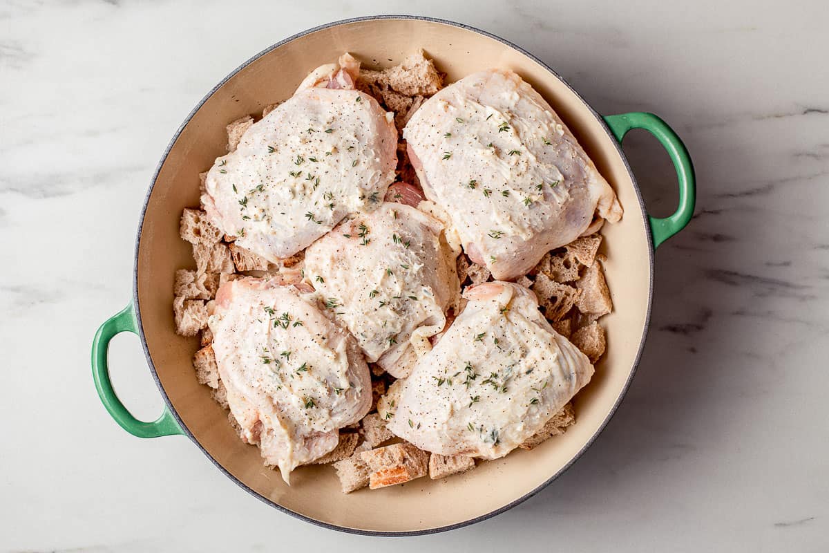 Raw chicken thighs with croutons in a skillet.