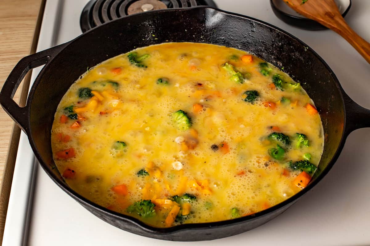 Eggs poured into a skillet over frittata ingredients.