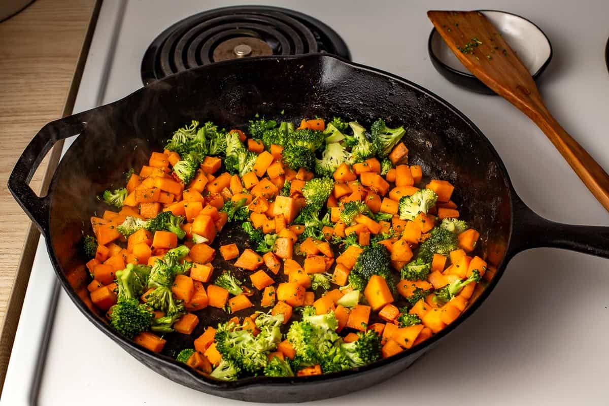 Sweet potato and broccoli cooking in a skillet on the stovetop.