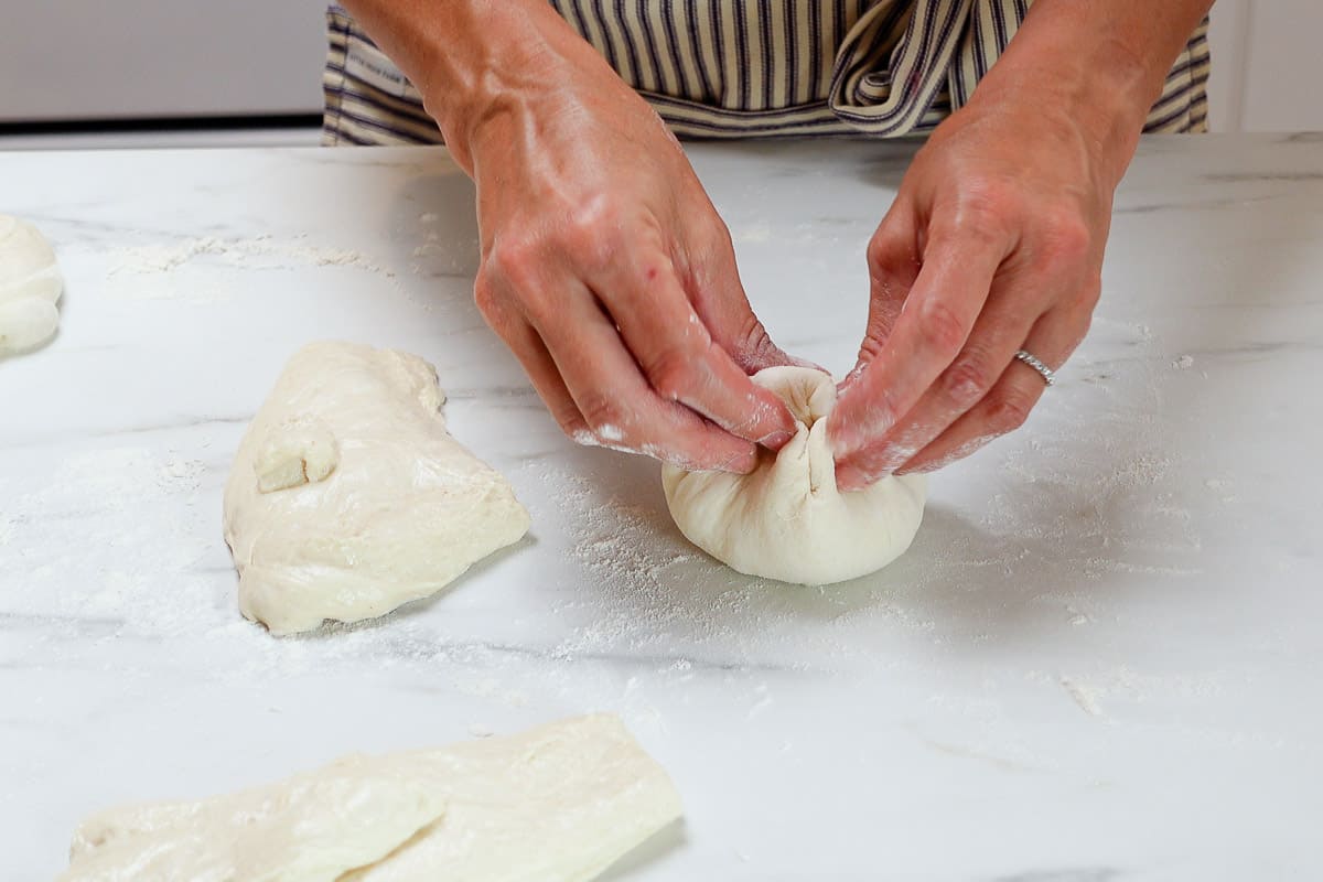 A woman pulling the sides of the dough up.