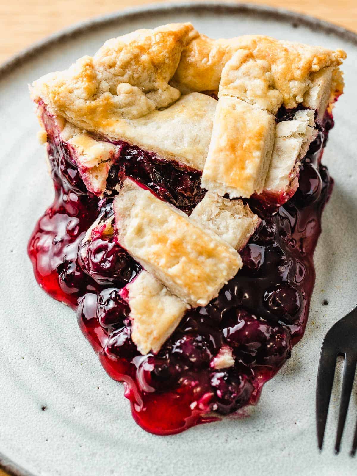 A slice of blueberry pie on a plate with a fork.