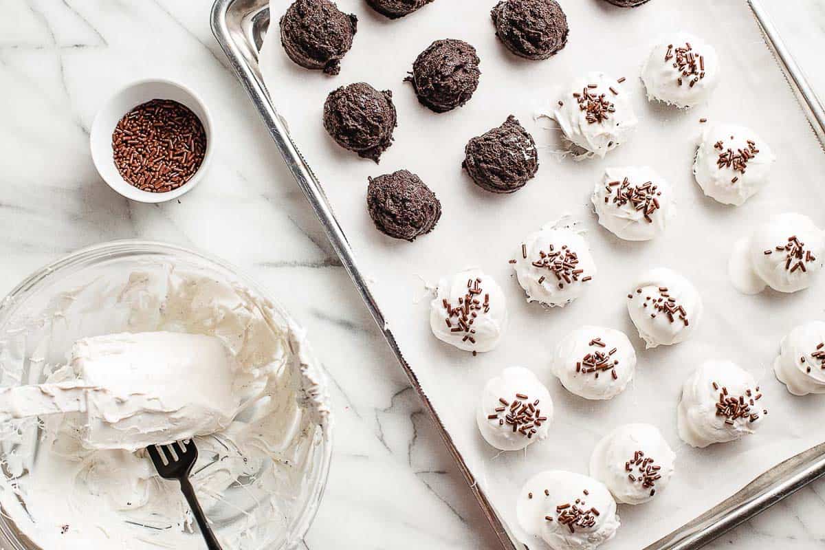 Scoops of oreo ball mixture covered in white chocolate on a baking sheet.