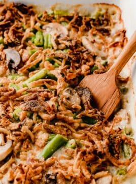 Green bean casserole in a baking dish with a wooden serving spoon.