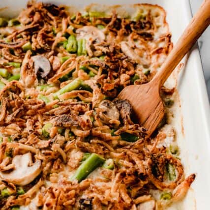 Green bean casserole in a baking dish with a wooden serving spoon.