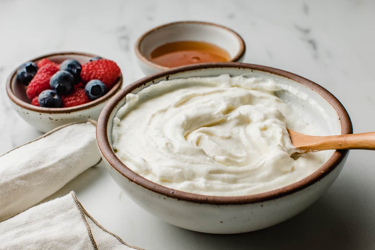 Raw yogurt in a bowl with a side of berries and honey.