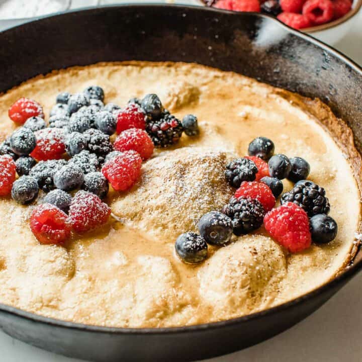 Sourdough dutch baby in a cast iron skillet topped with berries.