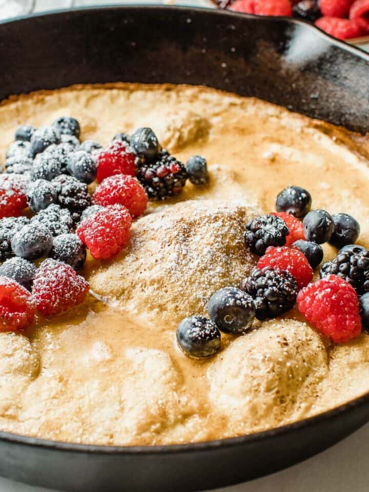 Sourdough dutch baby in a cast iron skillet topped with berries.