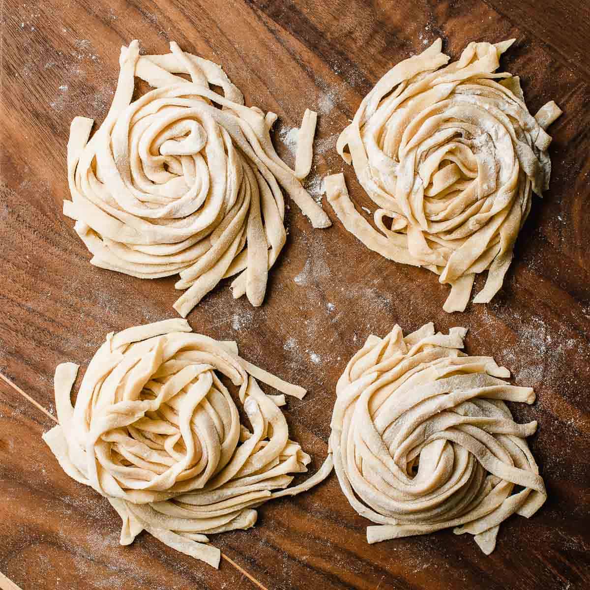 Four piles of fresh sourdough pasta on a cutting board.