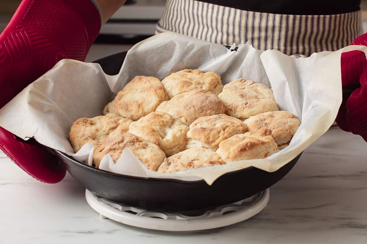 A woman holding a cast iron skillet with baked shortcake biscuits.