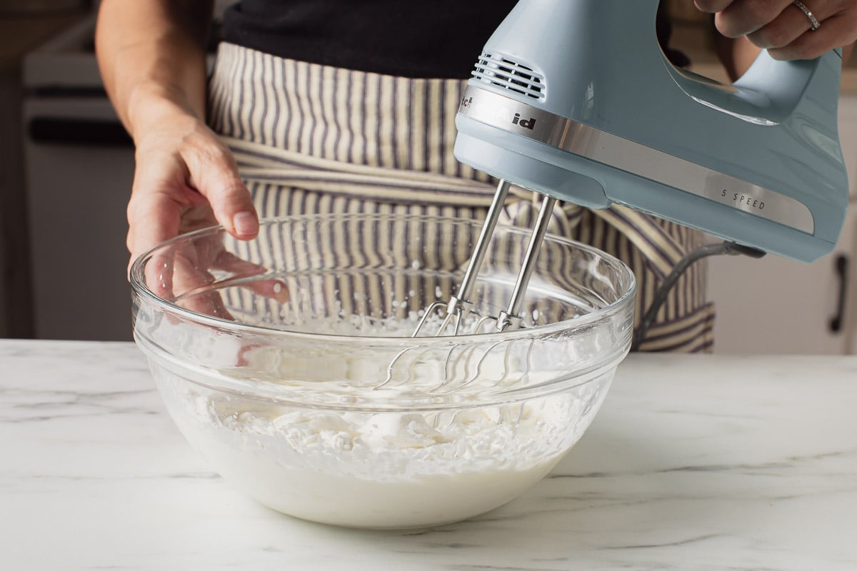 A woman making whipped cream with a hand mixer.