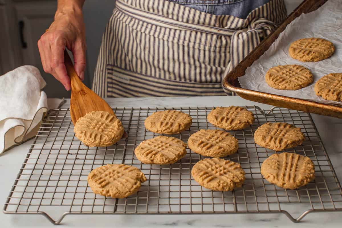 A woman placing cookies on a wire cooling rack.