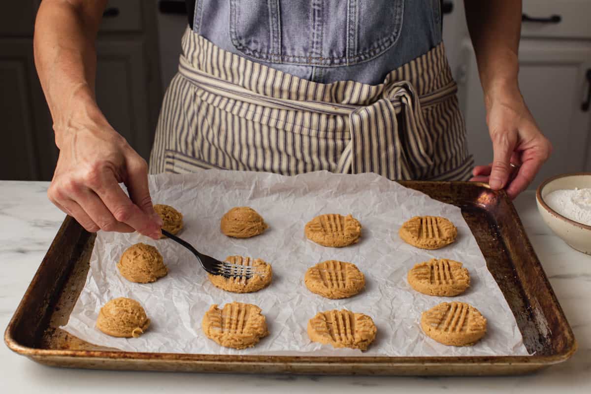 A woman pressing sourdough peanut butter cookie dough with a fork.