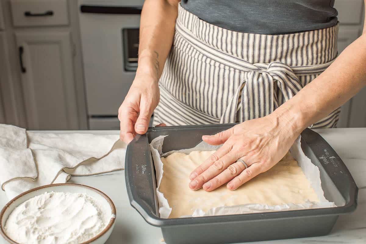 A woman pressing sourdough sugar cookie bar batter into a baking tin.