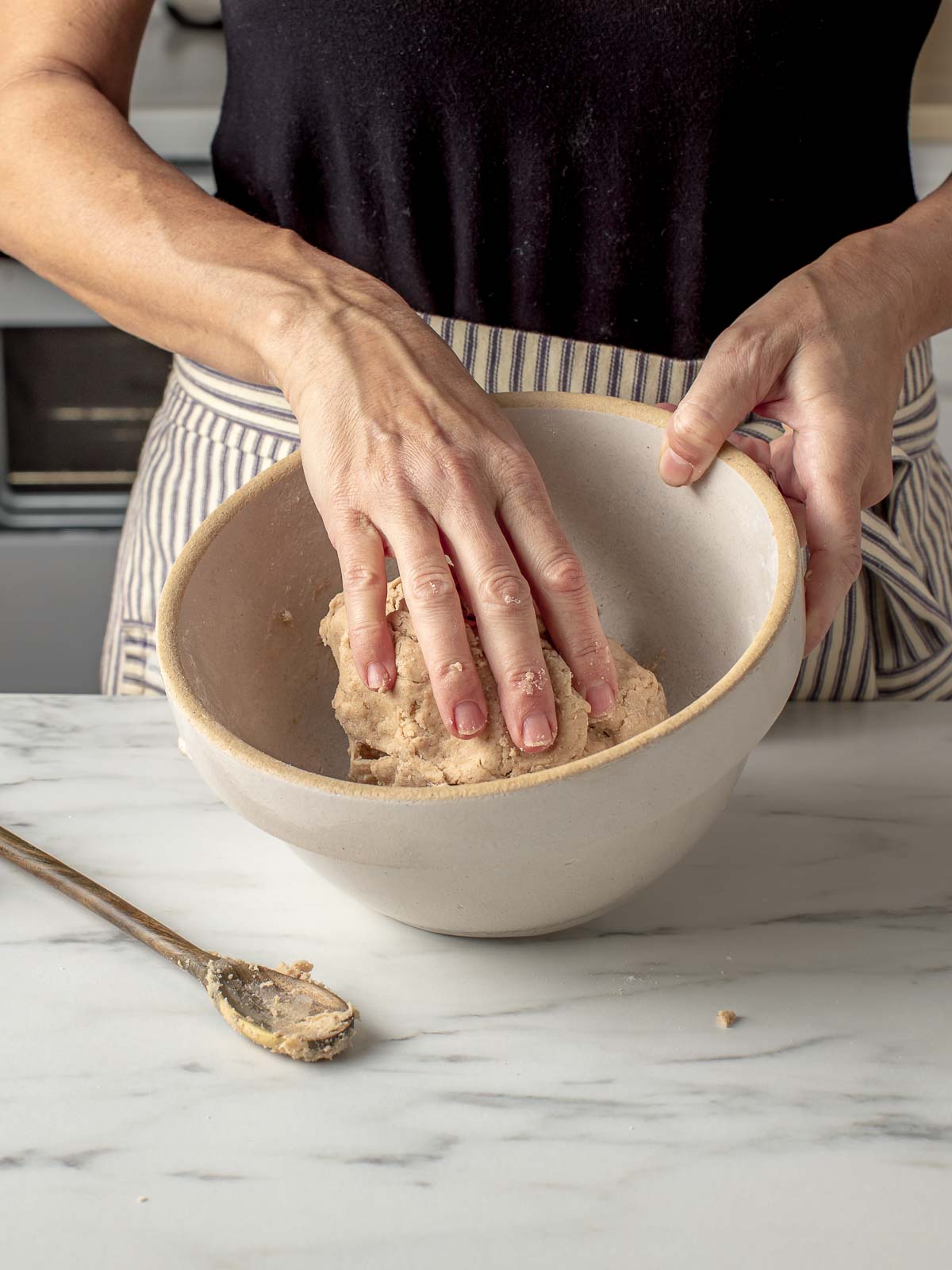 A woman using her hands to mix sourdough graham cracker dough.
