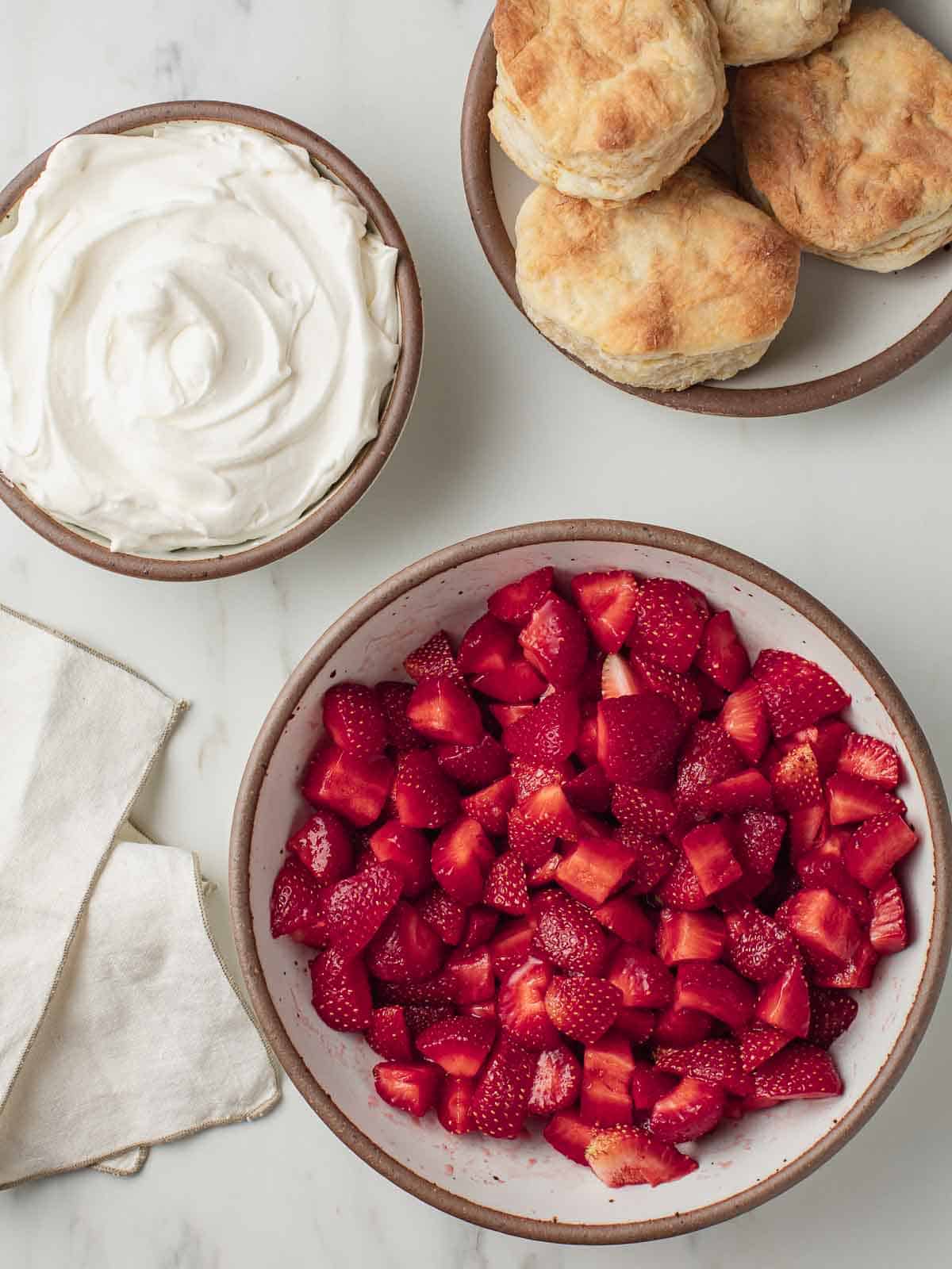 Three bowls with whipped cream strawberries and biscuits.