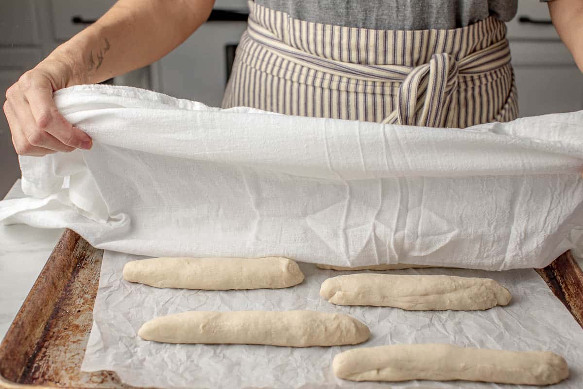A woman covering the breadstick dough with a tea towel.